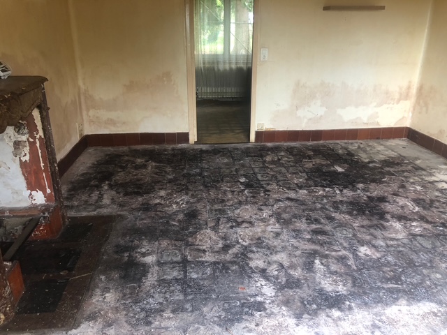 La salle à manger avant les travaux : sol noirci et détérioré, murs décapés, cheminée en ruine.